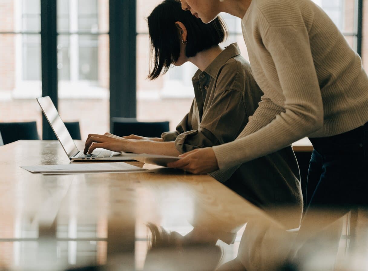 Een contentmarketeer typt een verzoek aan een AI-assistent op haar laptop, terwijl een collega meeleest
