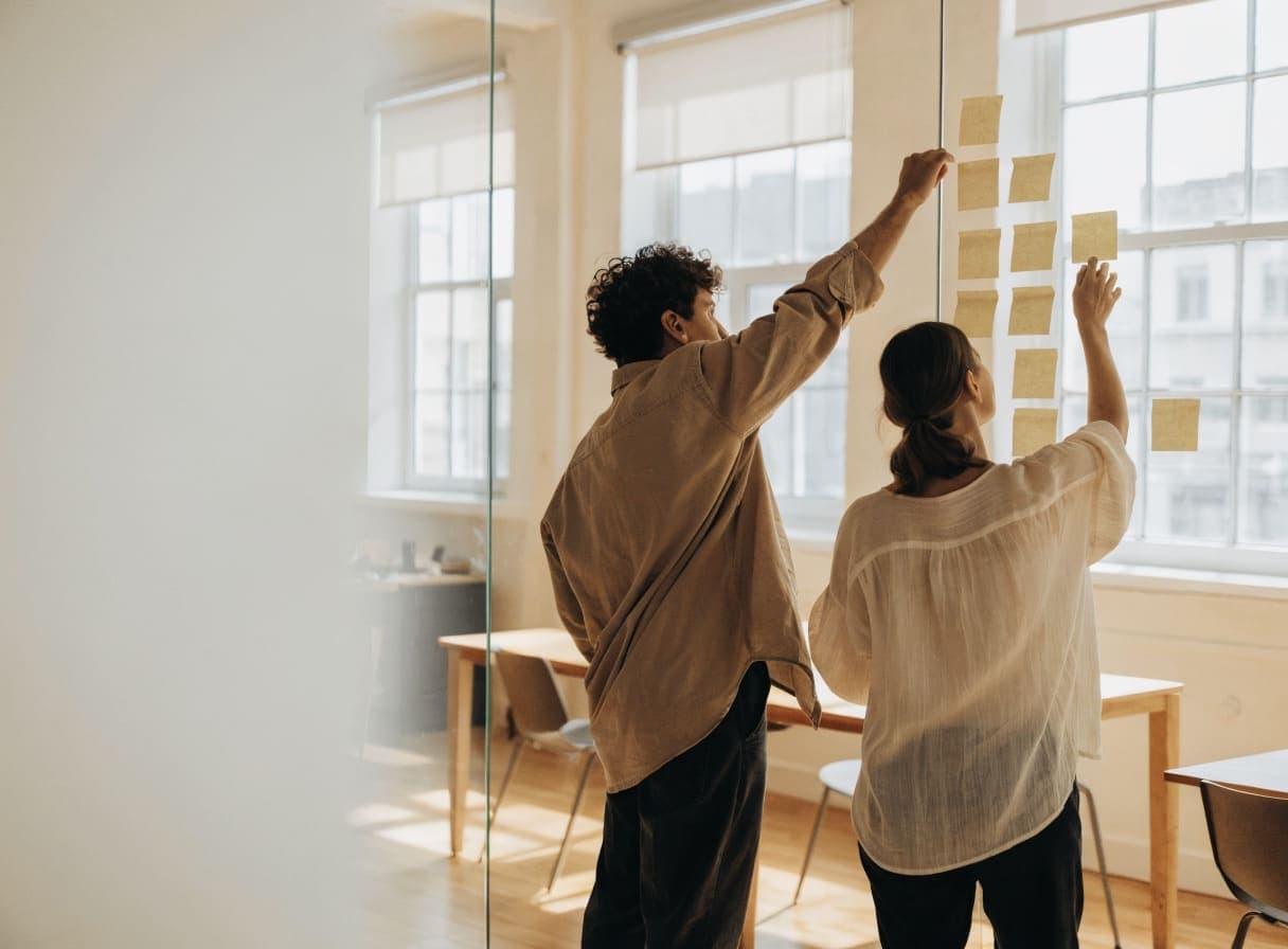 Twee mensen ordenen geeltjes op een glazen wand om de functies van een eerste productversie te prioriteren