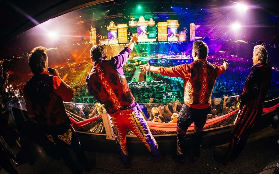 De Toppers zwaaien vanaf een podium in het publiek naar de zaal