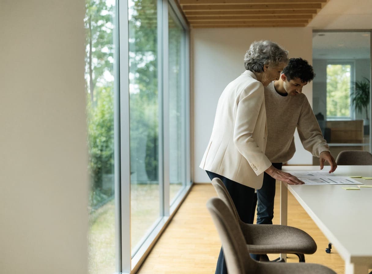 Twee collega's bekijken staand een overzicht dat op een tafel bij het raam ligt